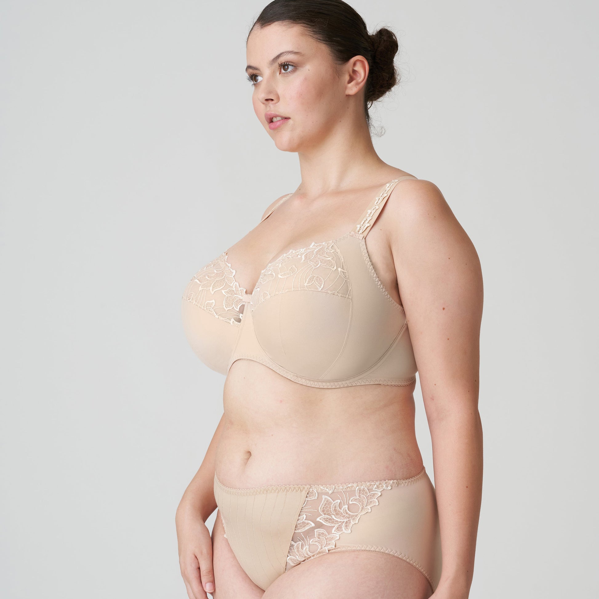 Woman wearing a beige bra and panties set on a plain background