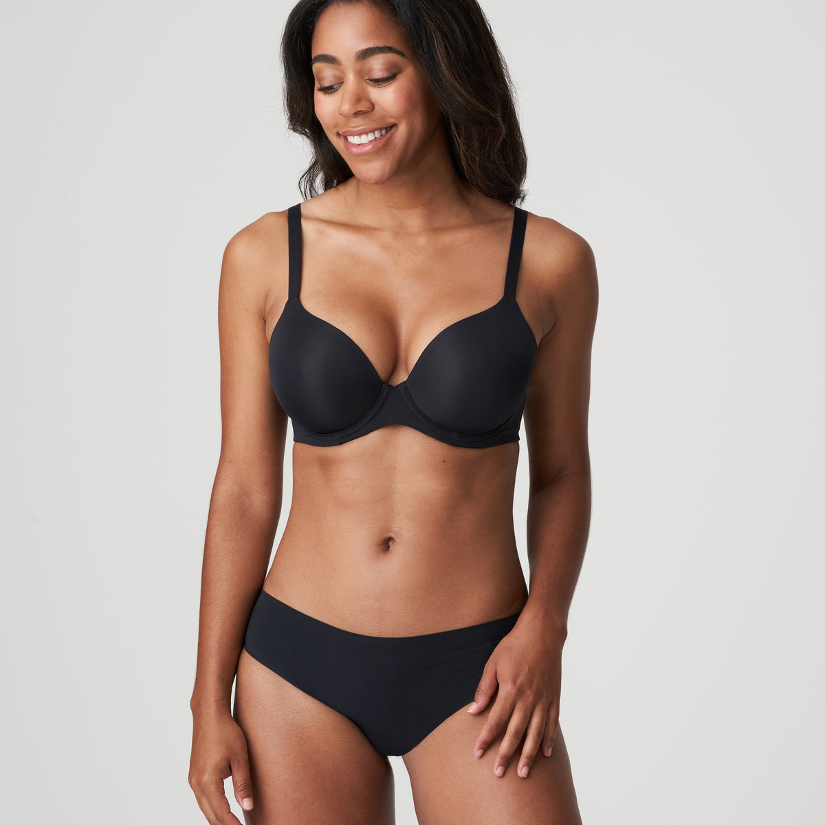 A woman wearing a charcoal Spacer Plunge Bra and matching briefs, standing against a white background.
