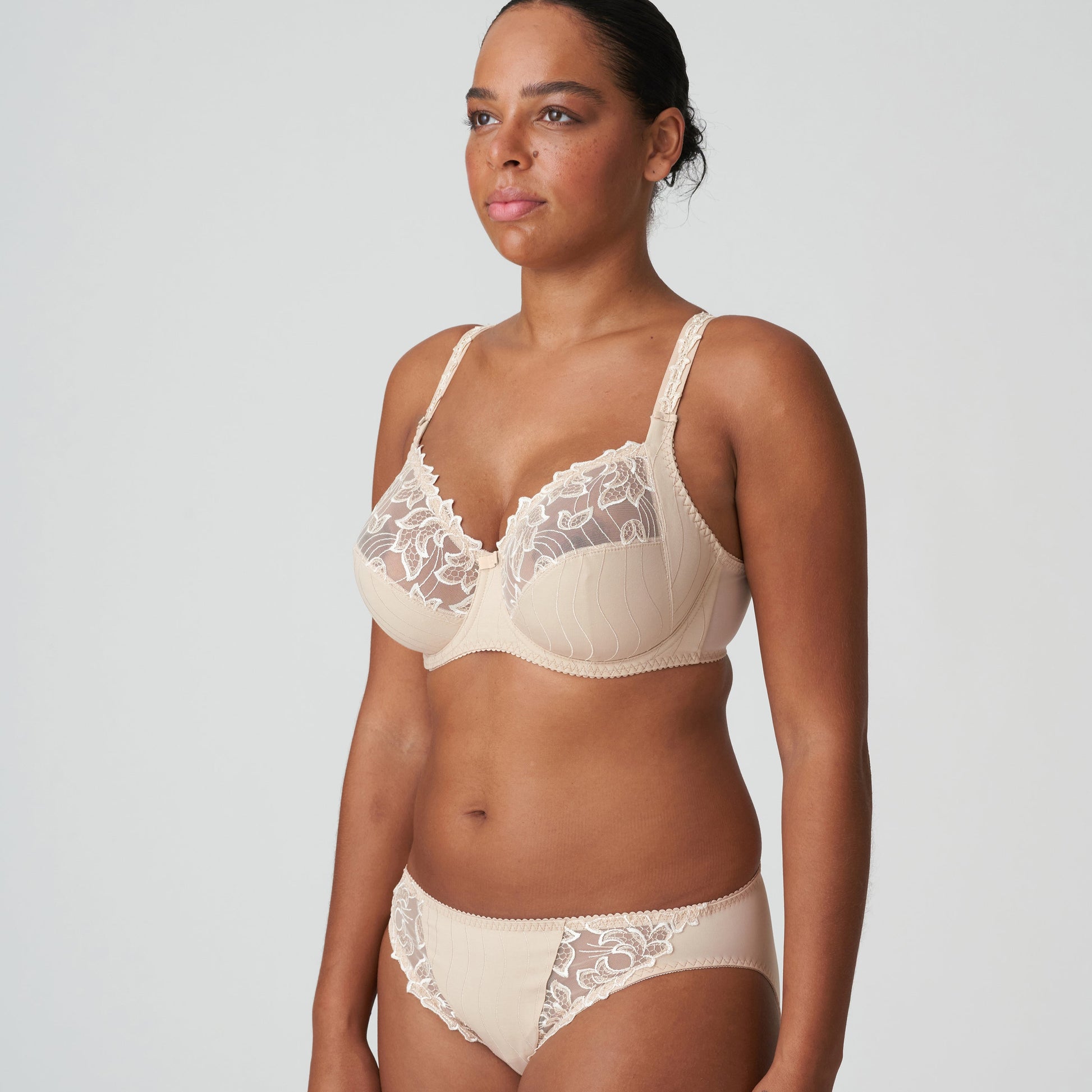 Woman wearing a beige bra and panties set with lace details on a plain background