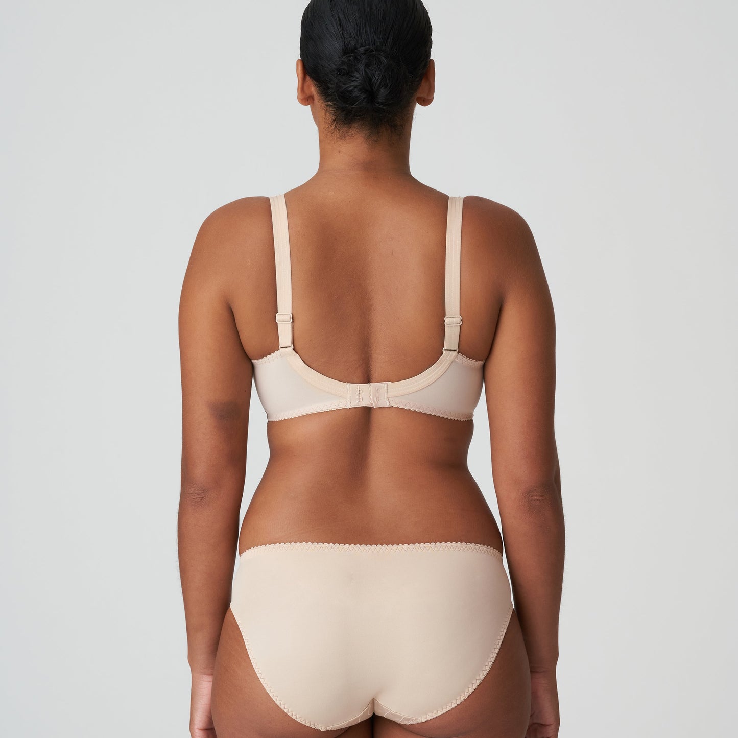Person wearing a beige bra and underwear set on a plain background