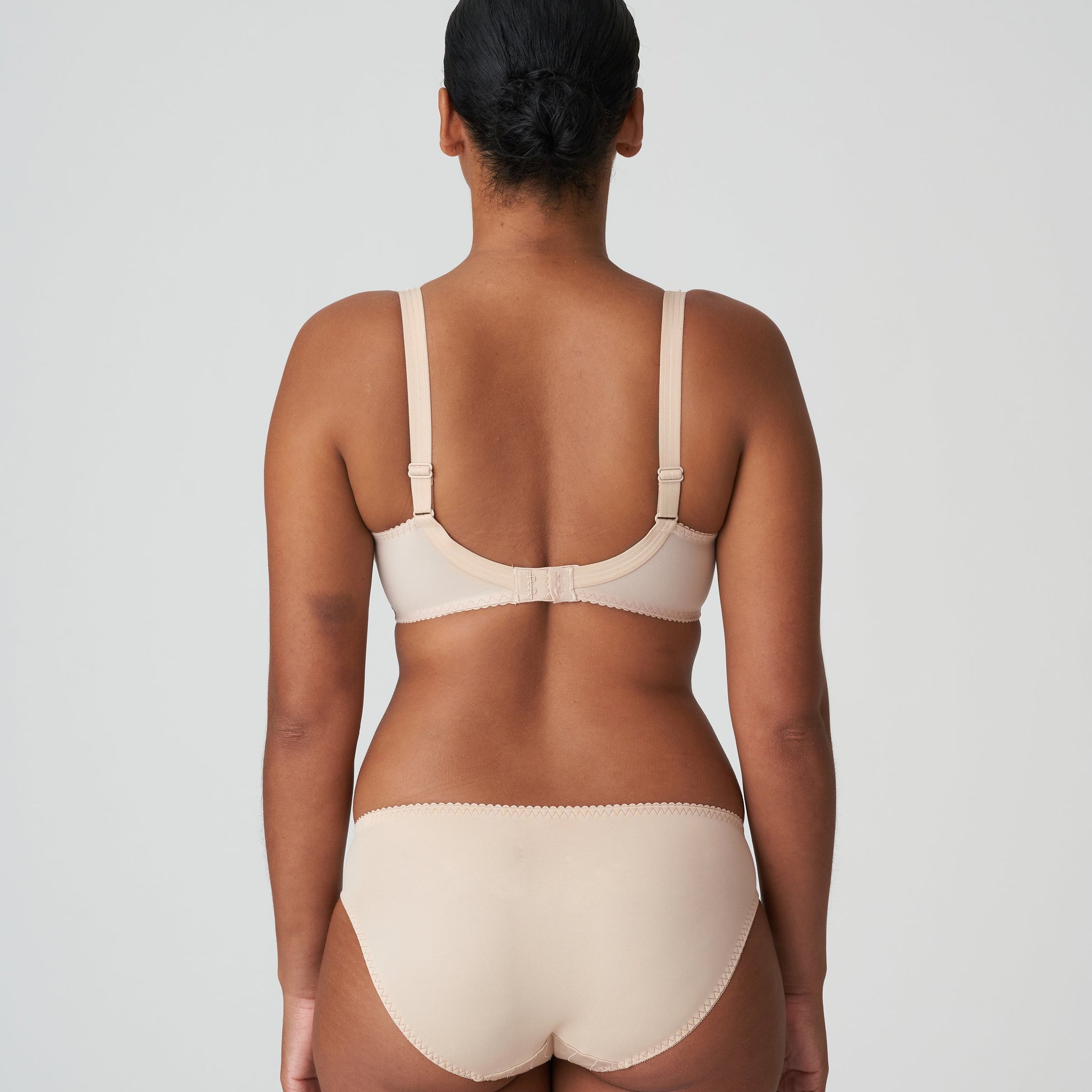 Person wearing a beige bra and underwear set on a plain background
