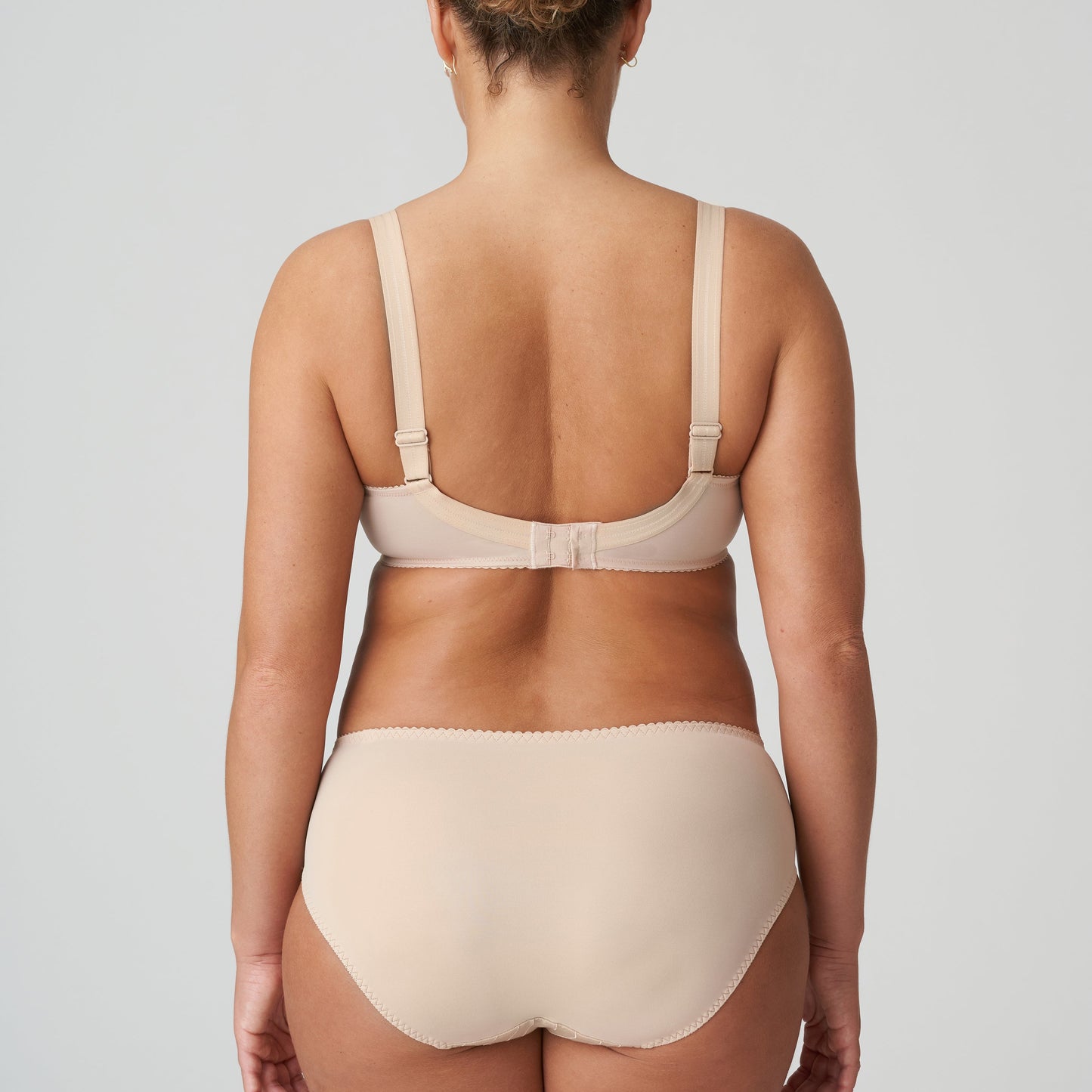 Person wearing a beige bra and underwear set on a plain background