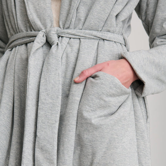 Close-up of a light gray heathered robe with a tie belt and front patch pocket, shown on a person whose hand is in the pocket.