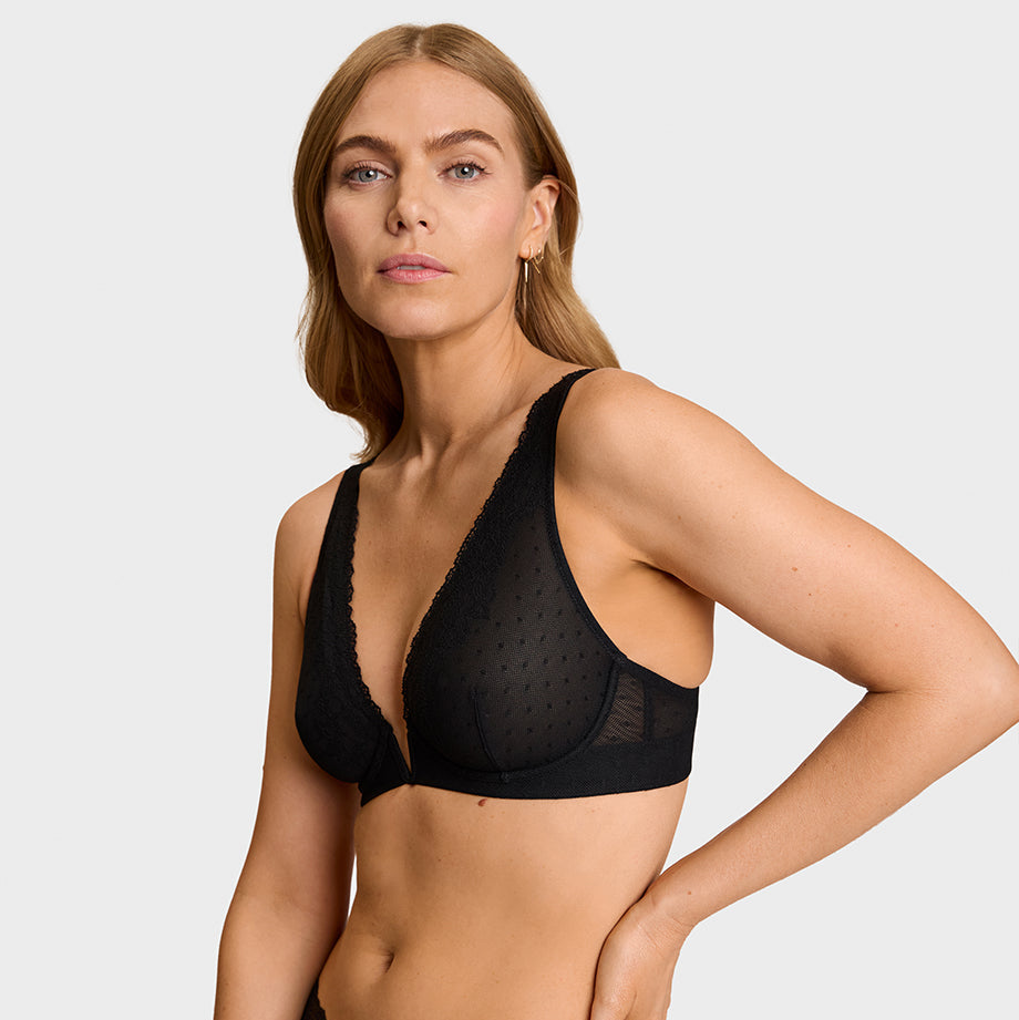 A woman modeling black sheer mesh and lace lingerie, featuring a V-neck bralette and matching high-waisted briefs, against a light gray studio background.