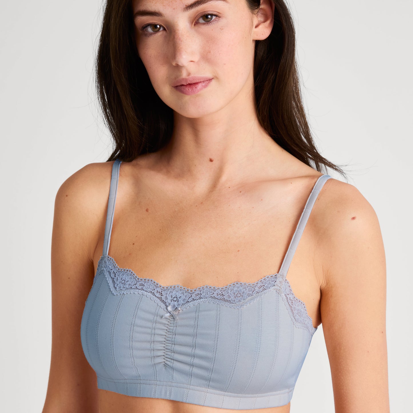 Woman wearing a light blue bralette with lace trim on a plain background
