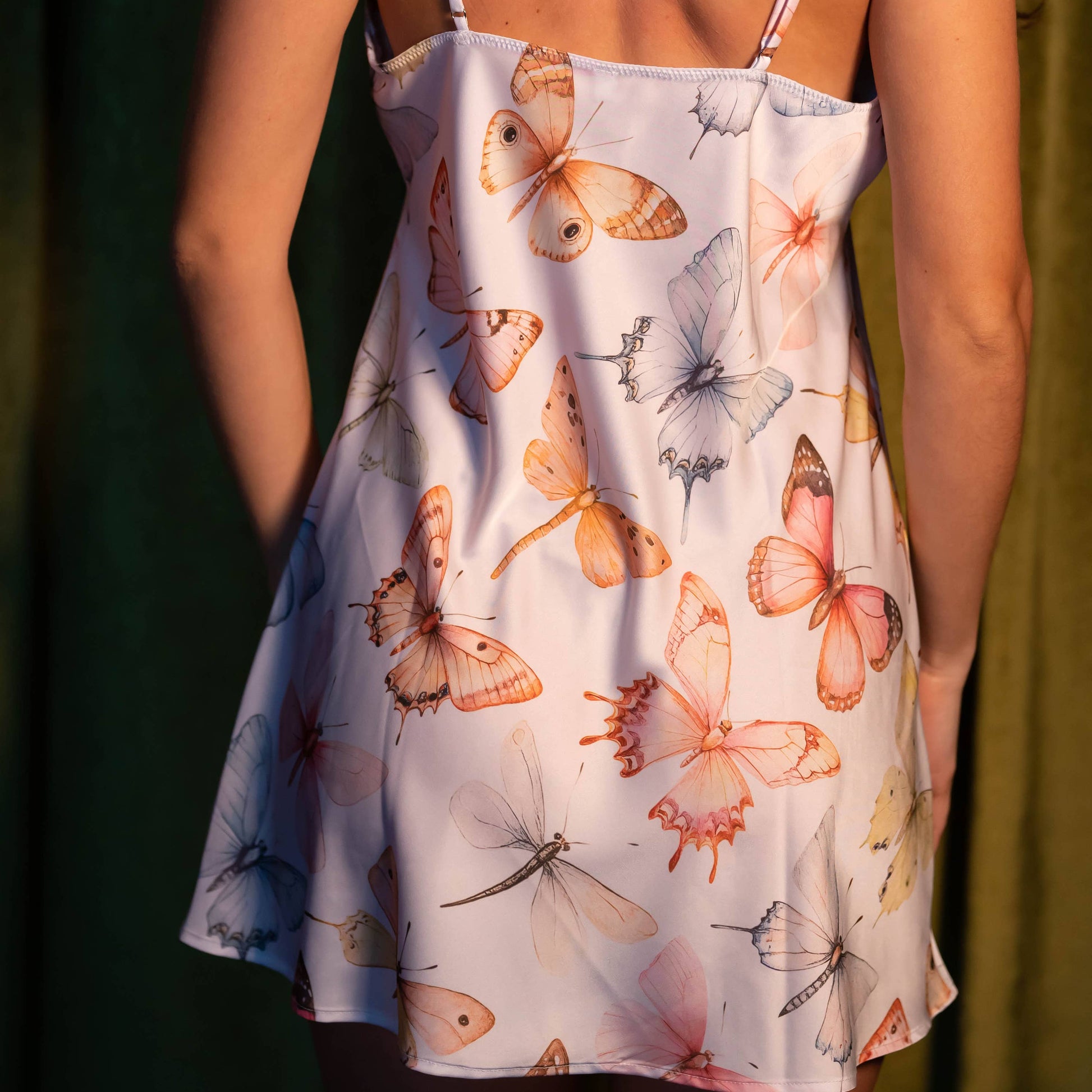Woman wearing a dress with butterfly pattern against a green curtain background