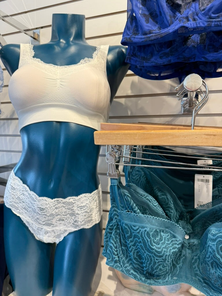 Mannequin wearing a white lace bra and panties with blue lingerie in the background.