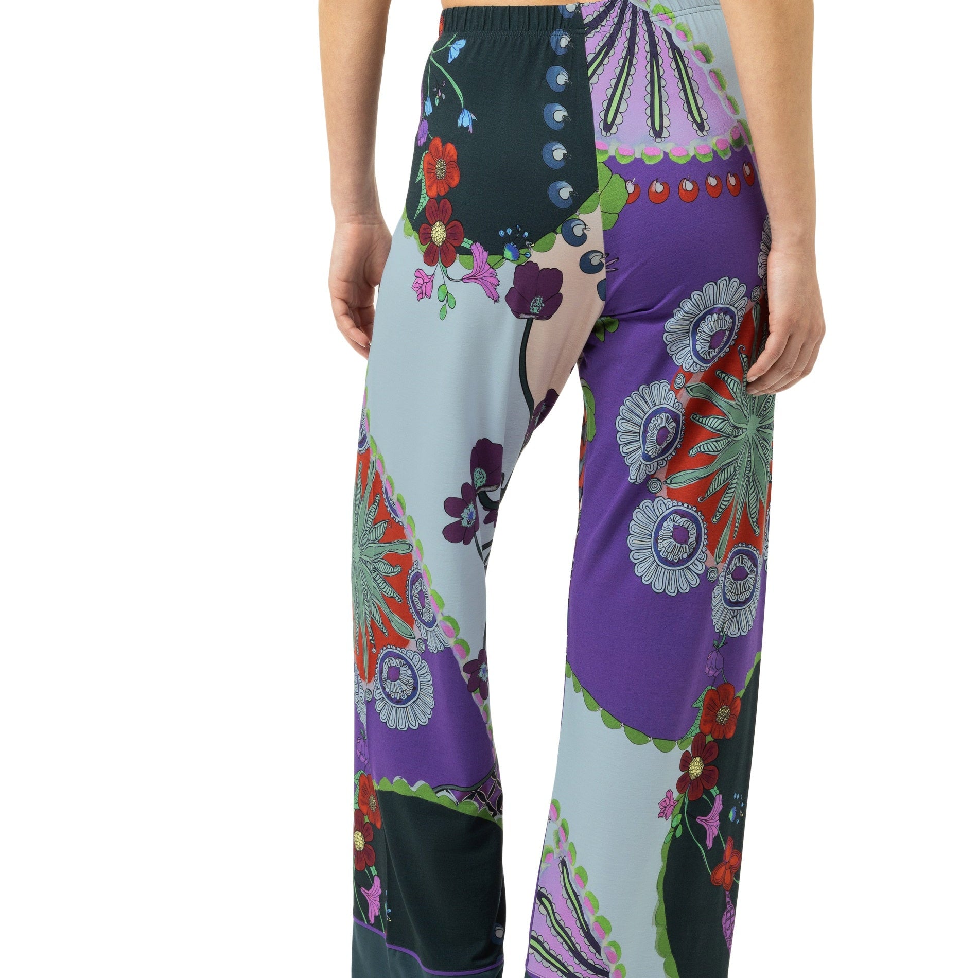 A model from the back wearing wide-leg pajama pants with a colorful patchwork bohemian floral print in purple, teal, green, and orange, paired with a purple bikini top against a white background.