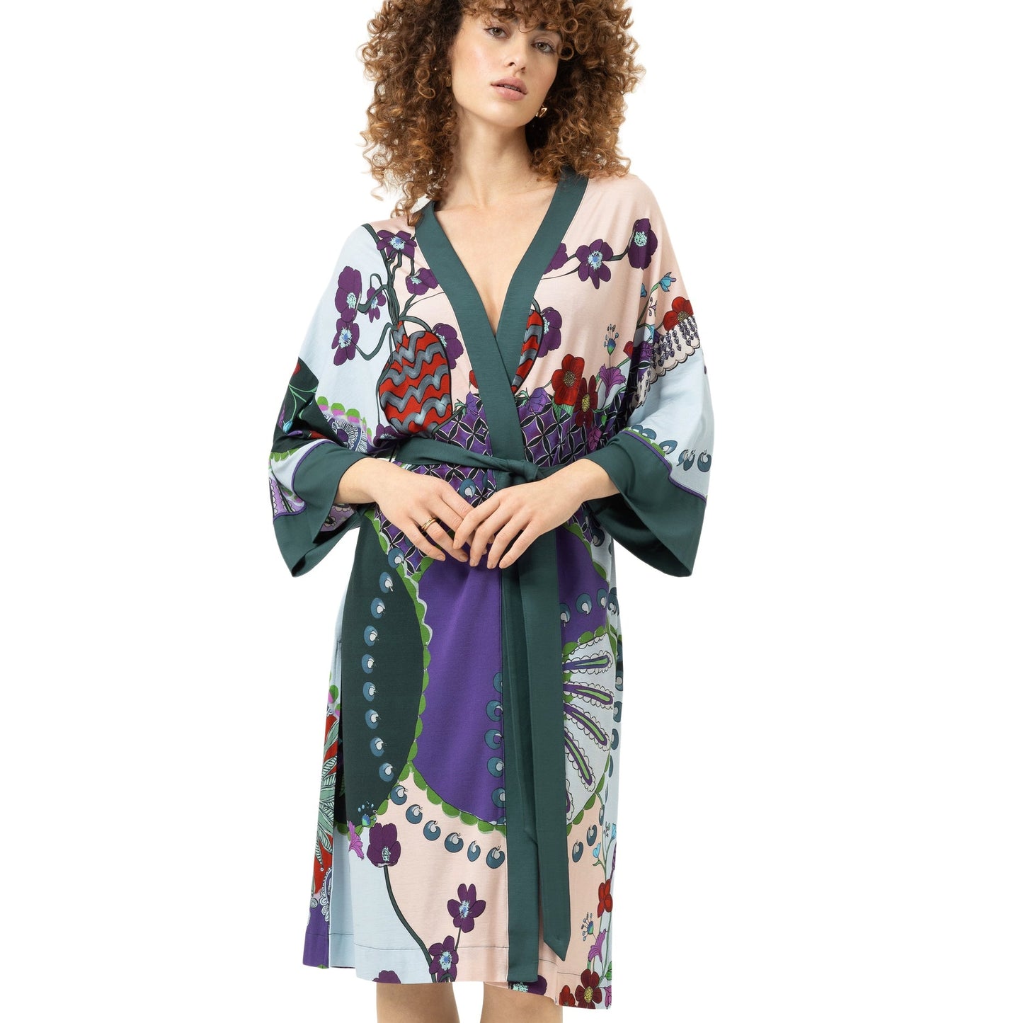 A woman wearing a long-sleeved wrap robe with a colorful patchwork print of purple, green, red, and beige floral motifs, set against a plain white background.