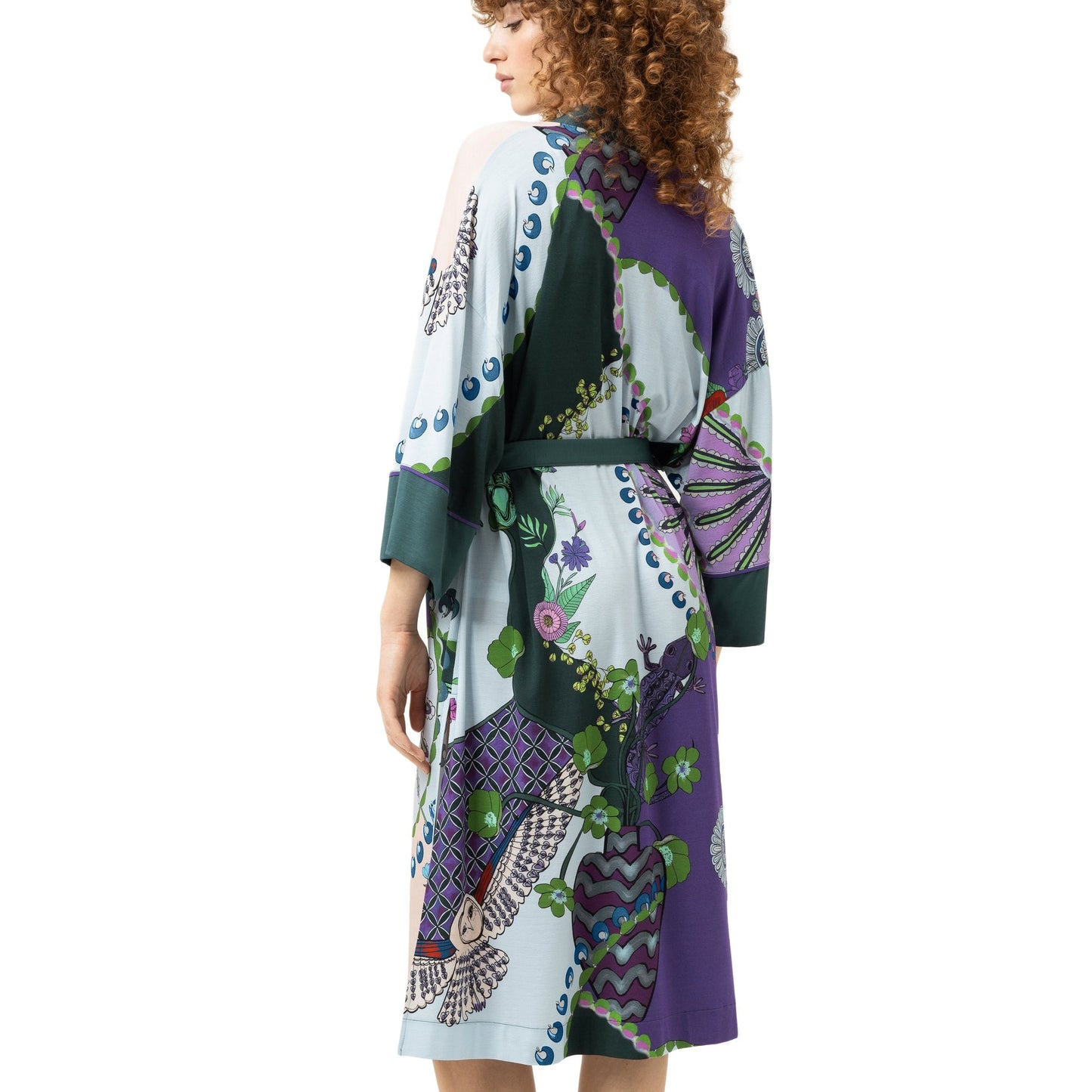 A woman with curly brown hair is shown from the back wearing a long-sleeved patchwork-print robe with a matching belt, standing against a plain white background.