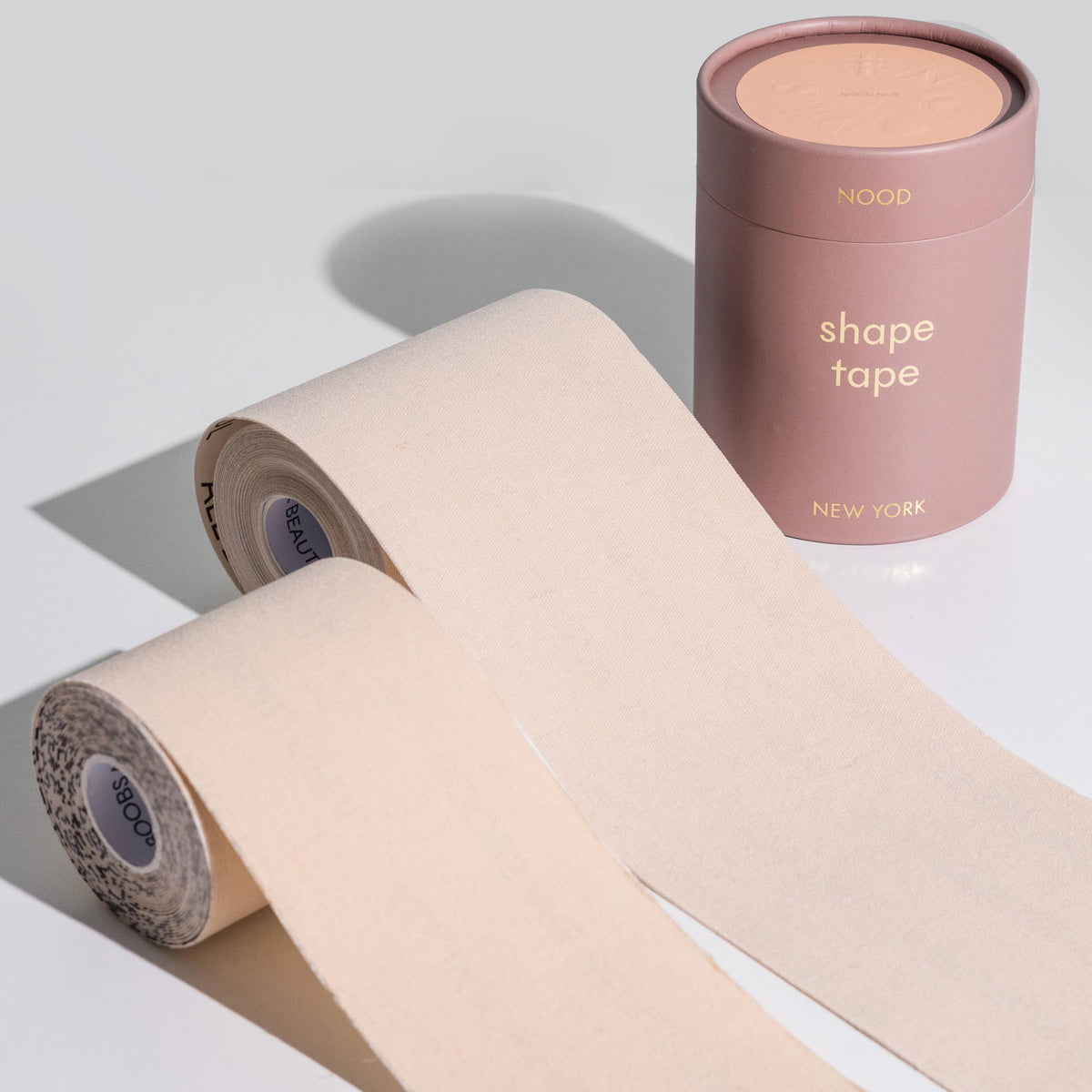 Two rolls of beige shape tape with a cylindrical container labeled 'shape tape' on a light gray background.