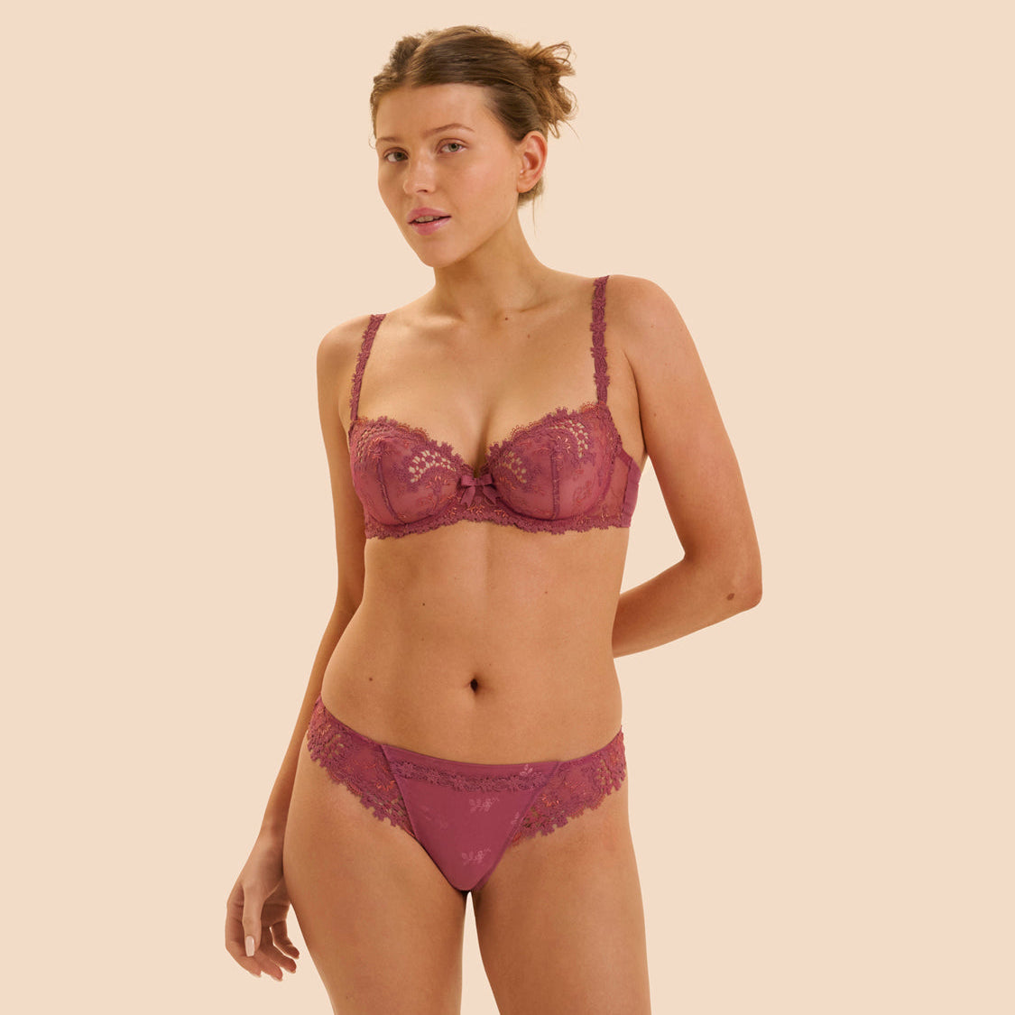 Woman wearing a maroon lace bra and panties set on a beige background