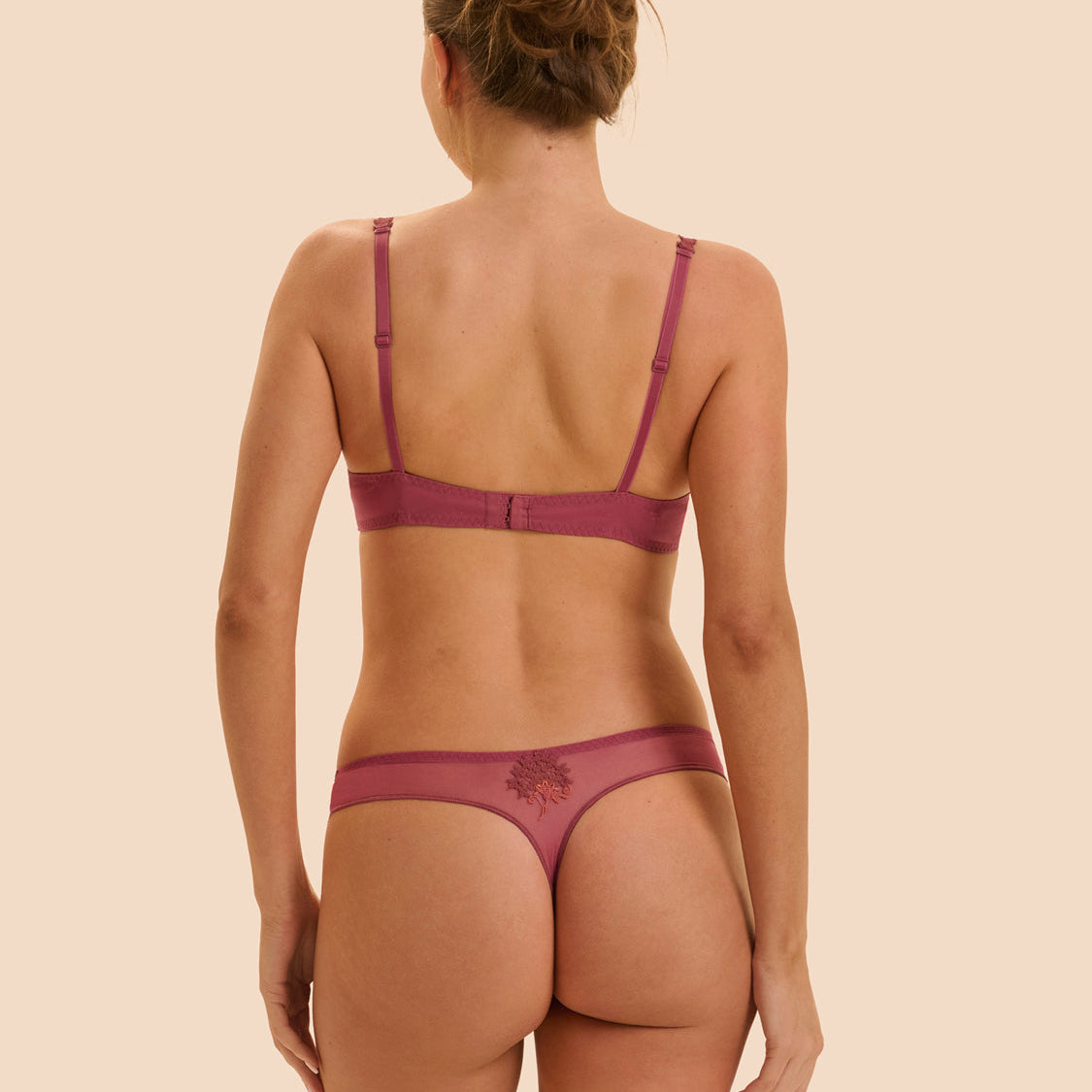 Woman wearing a maroon bra and panties set on a beige background