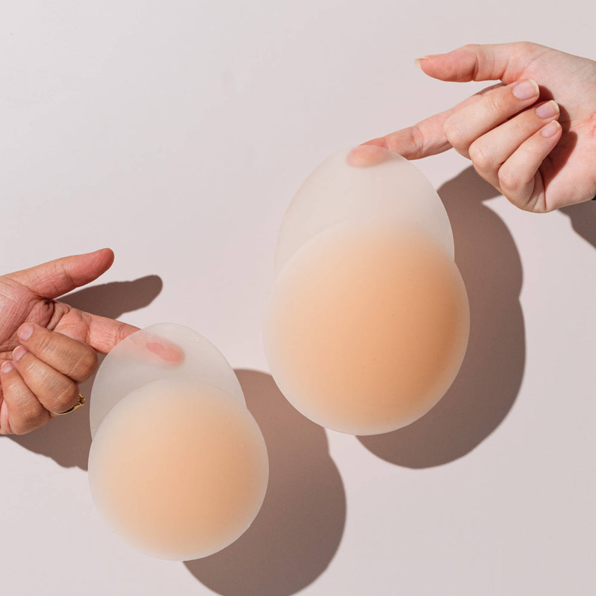 Two silicone breast forms held by hands on a light background