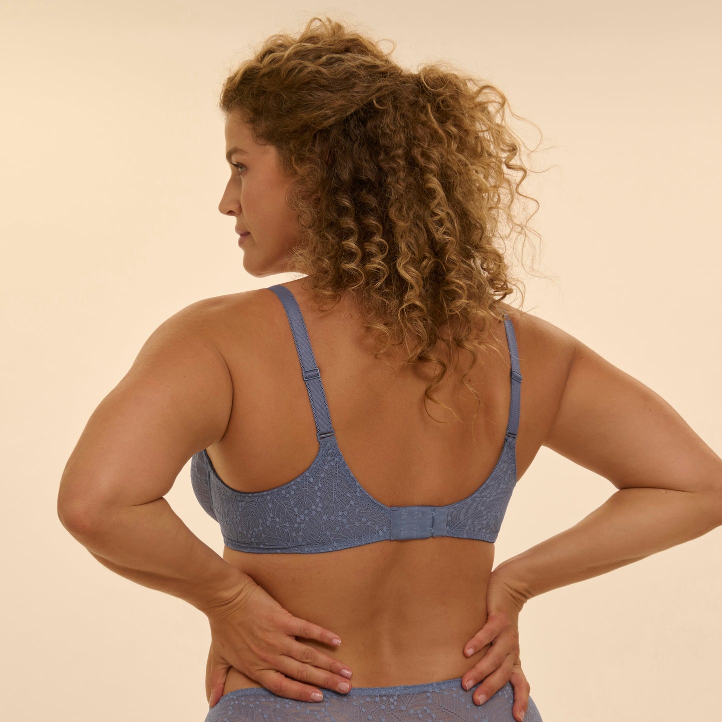 Woman wearing a blue bra and underwear against a beige background