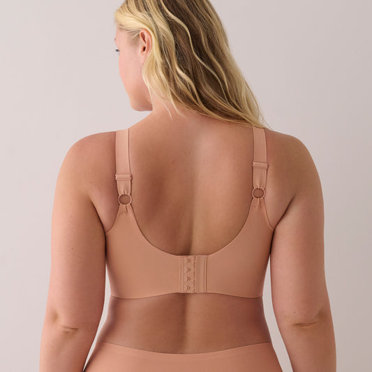A woman shown from the back wearing a seamless bra in a nude beige color, featuring adjustable shoulder straps with metal rings and a hook-and-eye closure at the center back.