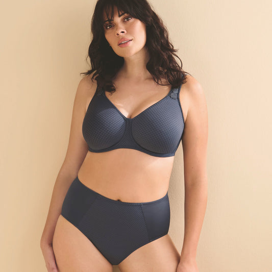 A woman modeling a dark gray two-piece lingerie set consisting of a textured underwire bra and matching high-waisted briefs, posed against a solid beige background.