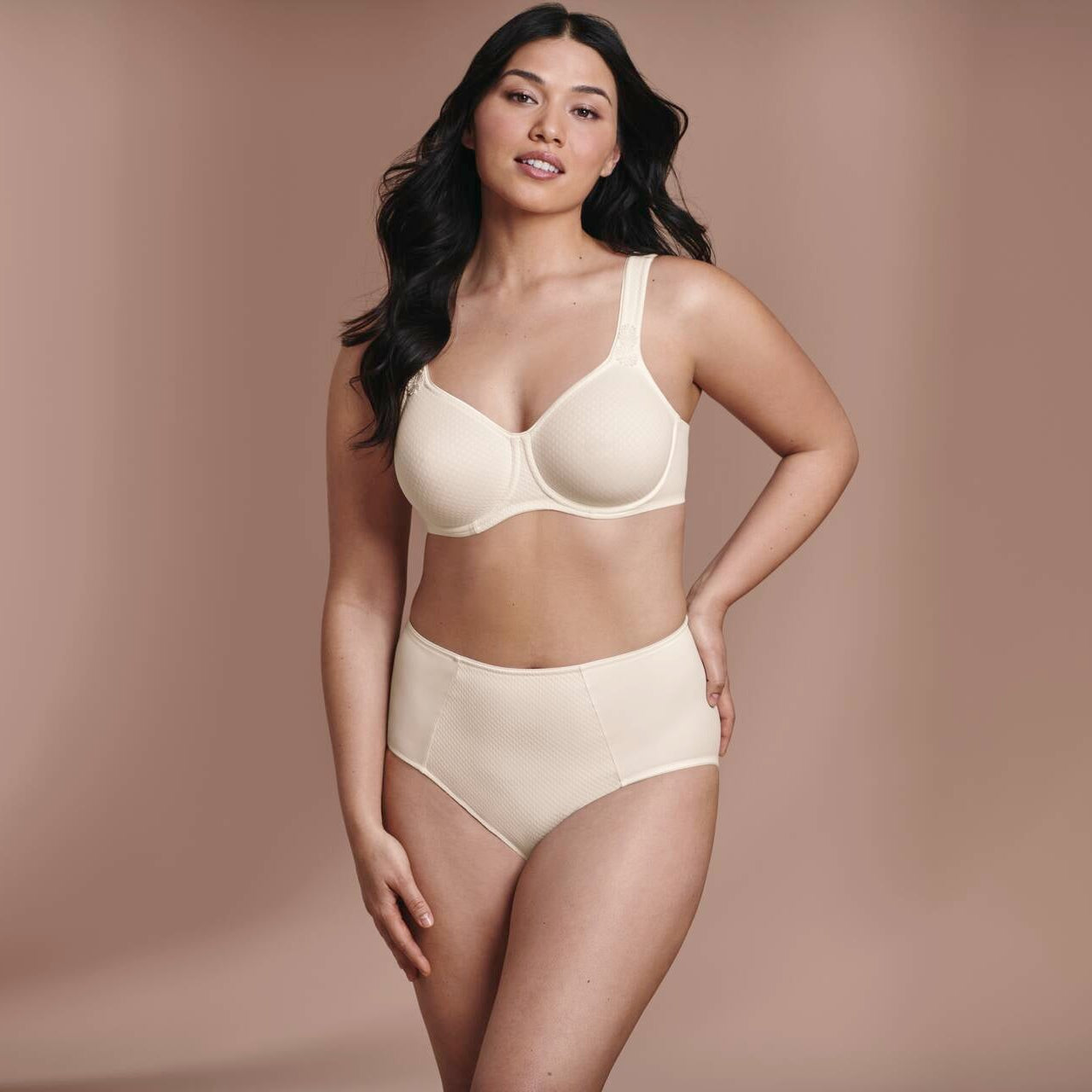 Woman wearing a beige bra and panties set against a brown background
