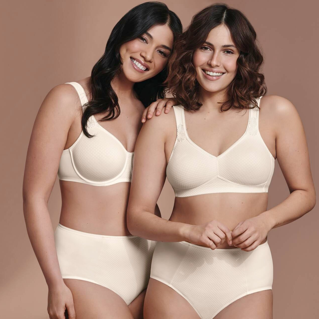 Two women wearing beige bras and panties against a brown background
