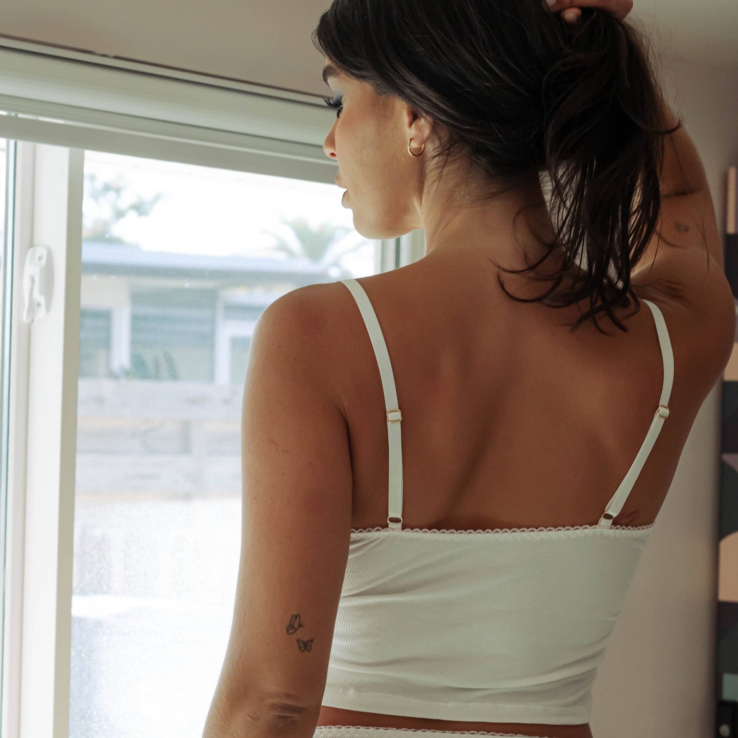 Woman wearing a white bikini standing by a window.
