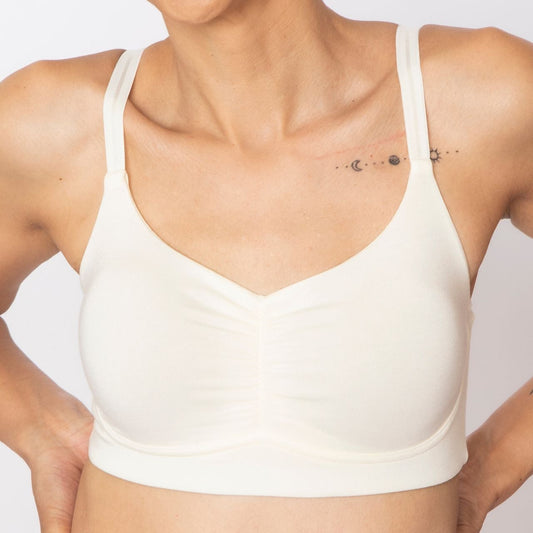 A woman wearing a beige, full coverage, wire-free bra with a ruched front.