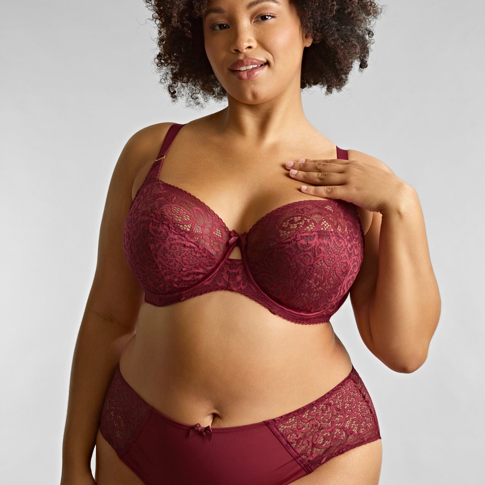 Woman wearing a maroon lace lingerie set against a plain background