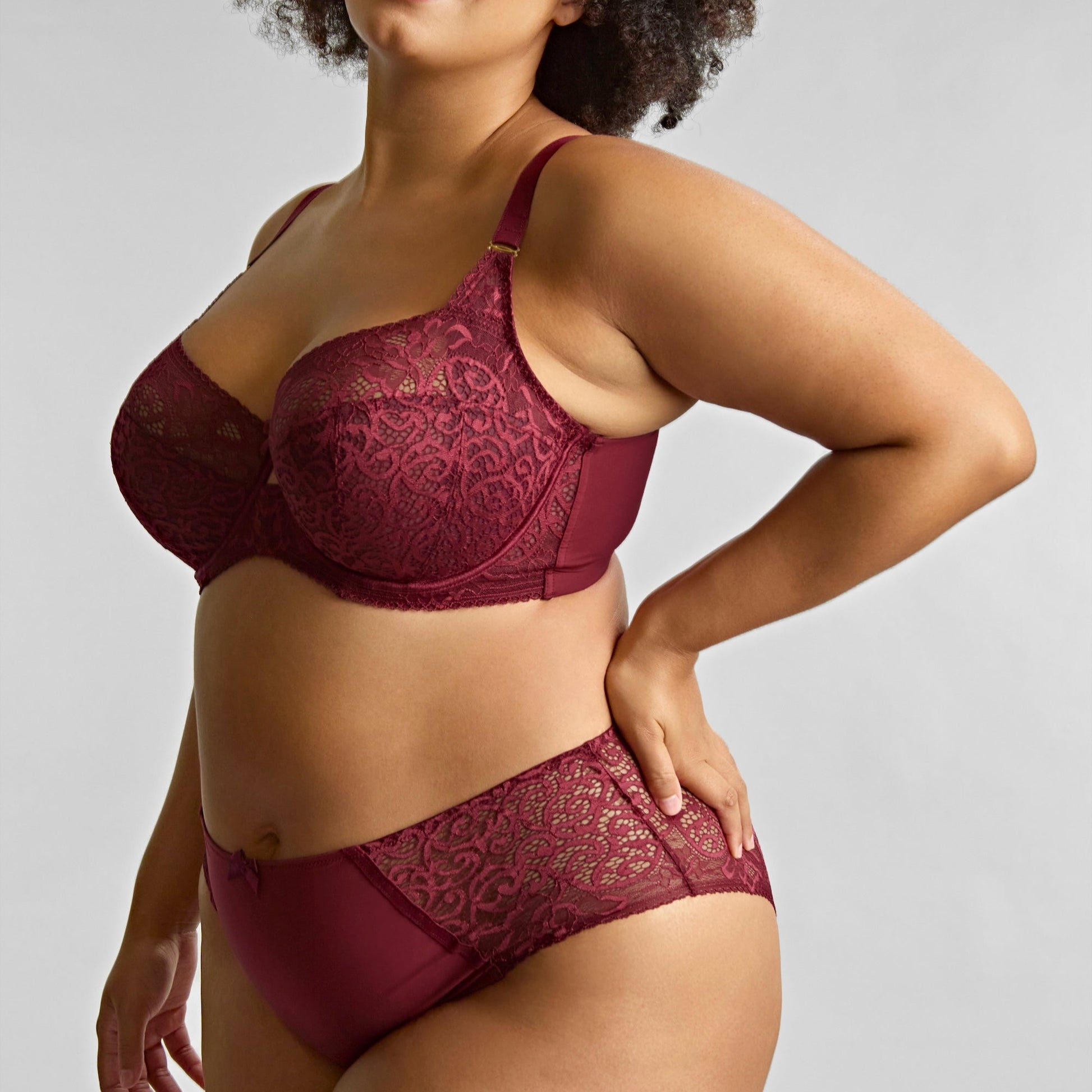 Woman wearing a burgundy lace lingerie set against a plain background