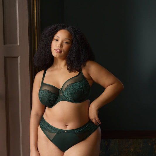 Woman wearing a green lingerie set in a dimly lit room.