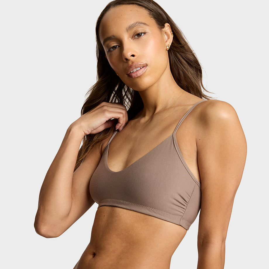 A woman modeling a matching taupe-brown bikini set against a light gray studio background.
