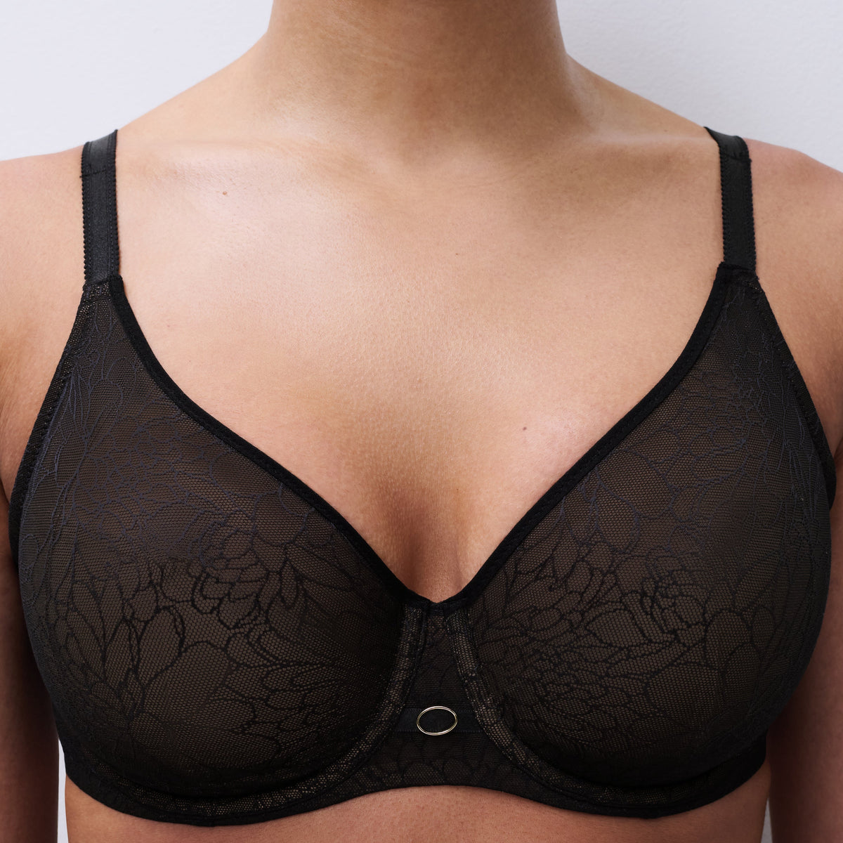 A close-up of a model wearing a black sheer lace underwire bra with floral patterns and adjustable shoulder straps.