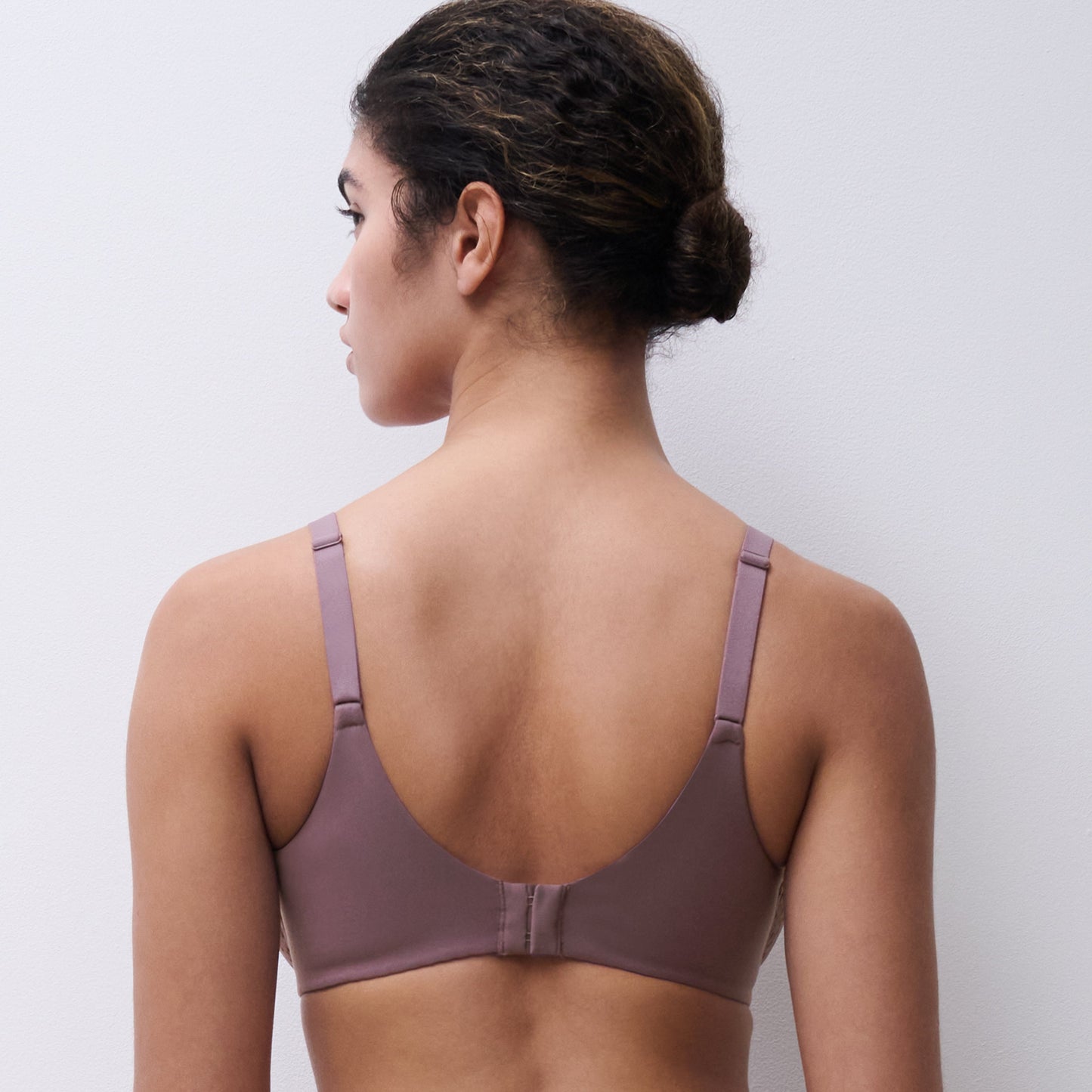 A woman shown from the back wearing a dusty mauve bralette and matching bottoms against a plain light gray studio background.