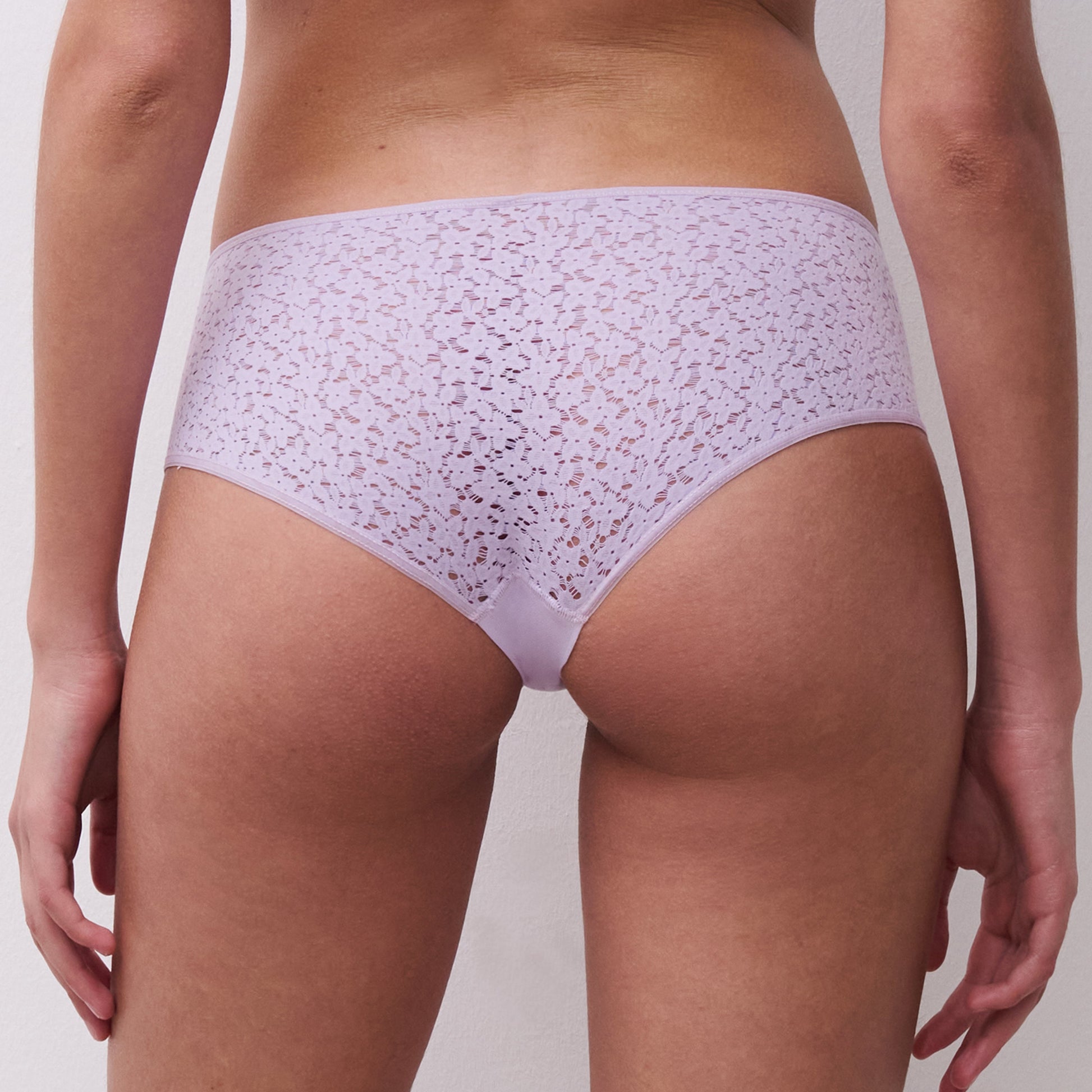 Person wearing a light purple lace underwear set on a plain background
