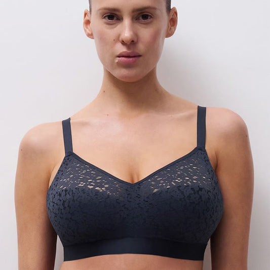A woman modeling a dark navy blue lace bralette against a plain light gray background.