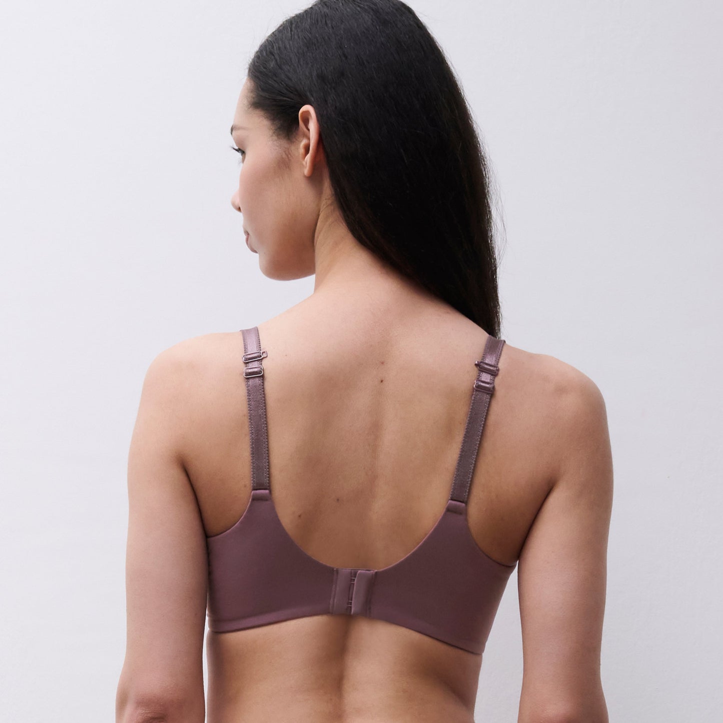 A woman shown from the back wearing a dusty mauve bra and matching underwear against a plain light gray studio background.