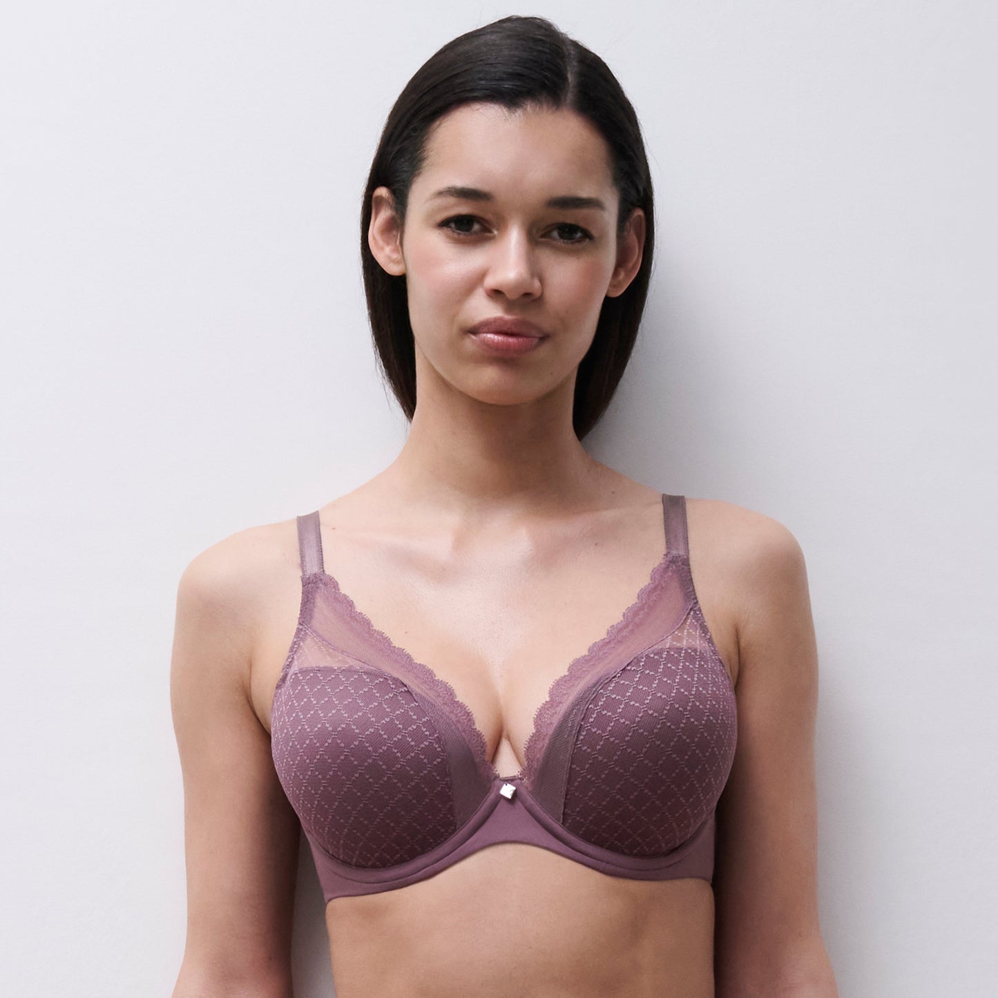 A woman modeling a dusty mauve underwire bra with a subtle diamond pattern and scalloped lace trim against a light gray background.