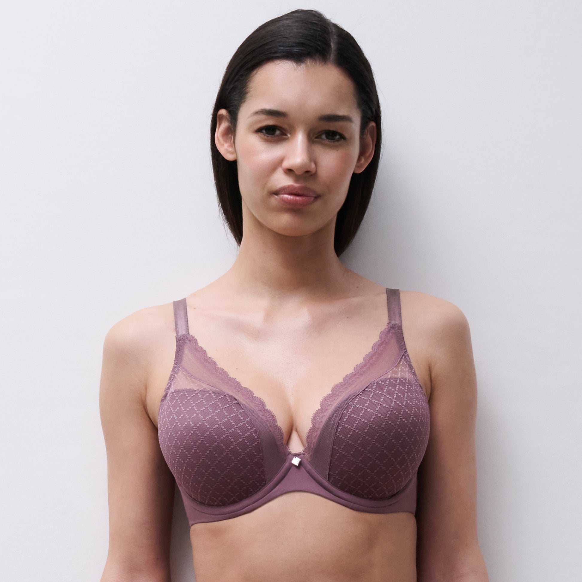 A woman modeling a dusty mauve underwire bra with a subtle diamond pattern and scalloped lace trim against a light gray background.