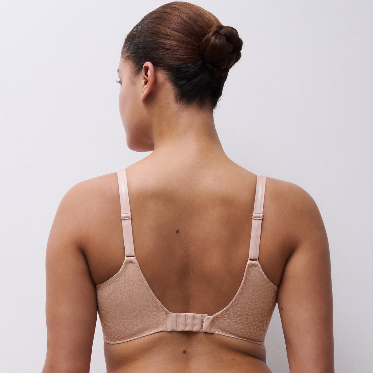 Woman wearing a beige bra and underwear set against a plain background
