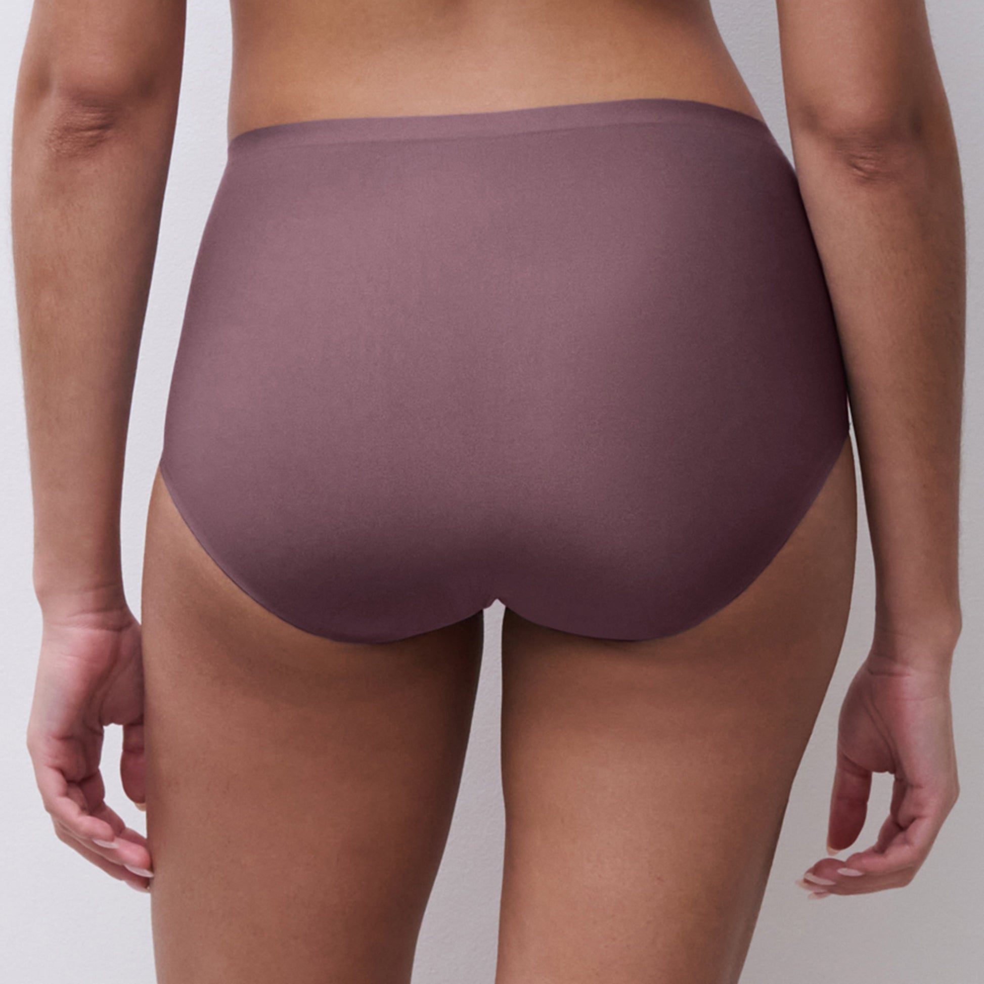 Rear view of a model wearing high-waisted, seamless underwear in a muted mauve-purple color, set against a plain light gray background.