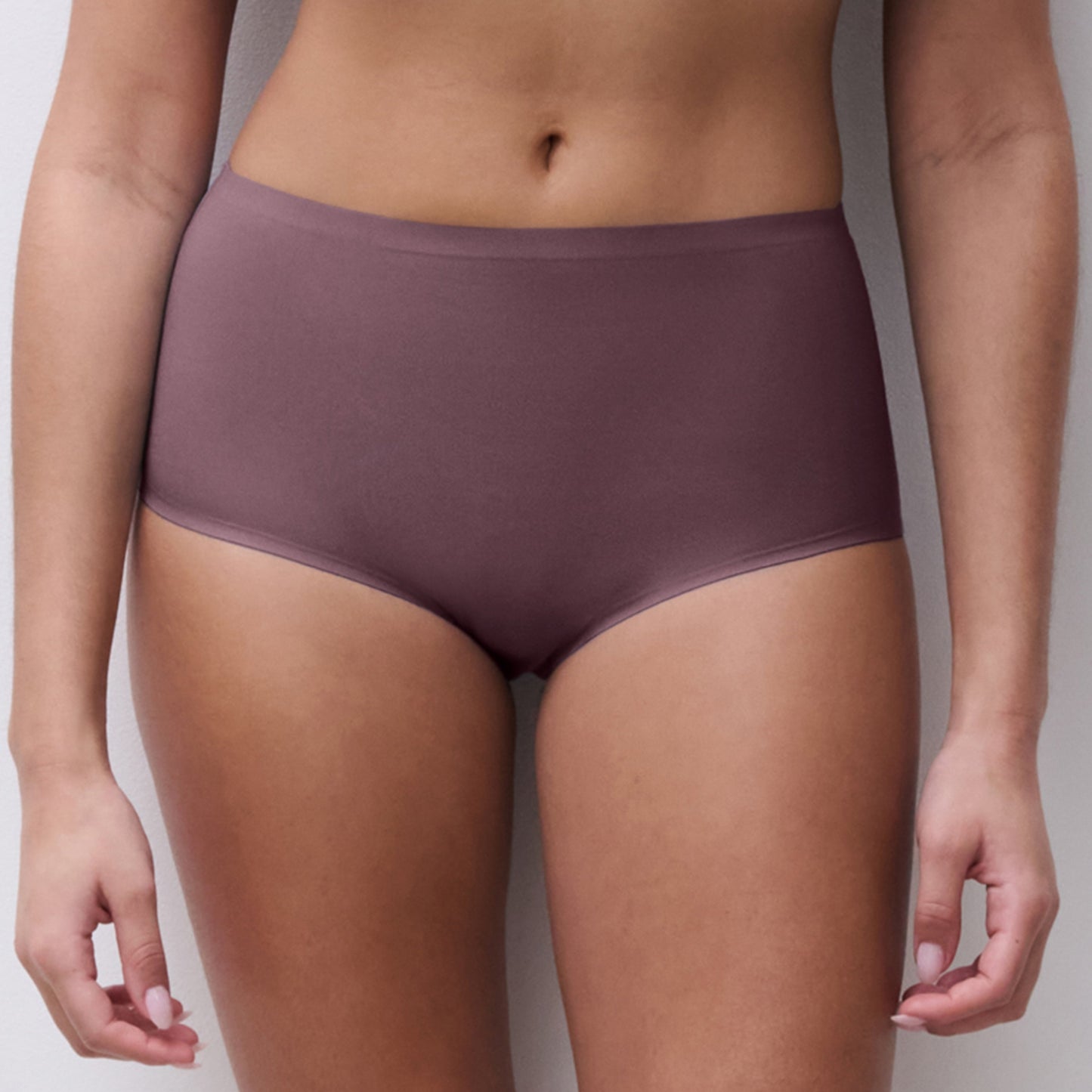 A model wearing high-waisted, seamless briefs in a muted mauve-purple color, shown from the waist to the upper thighs against a neutral light gray background.
