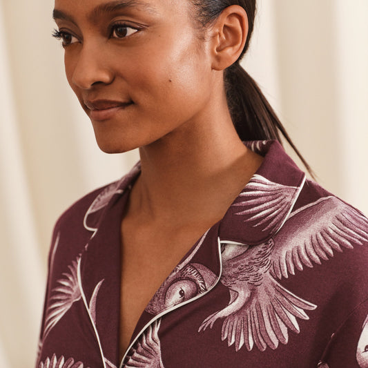 Woman wearing a maroon shirt with bird pattern against a neutral background
