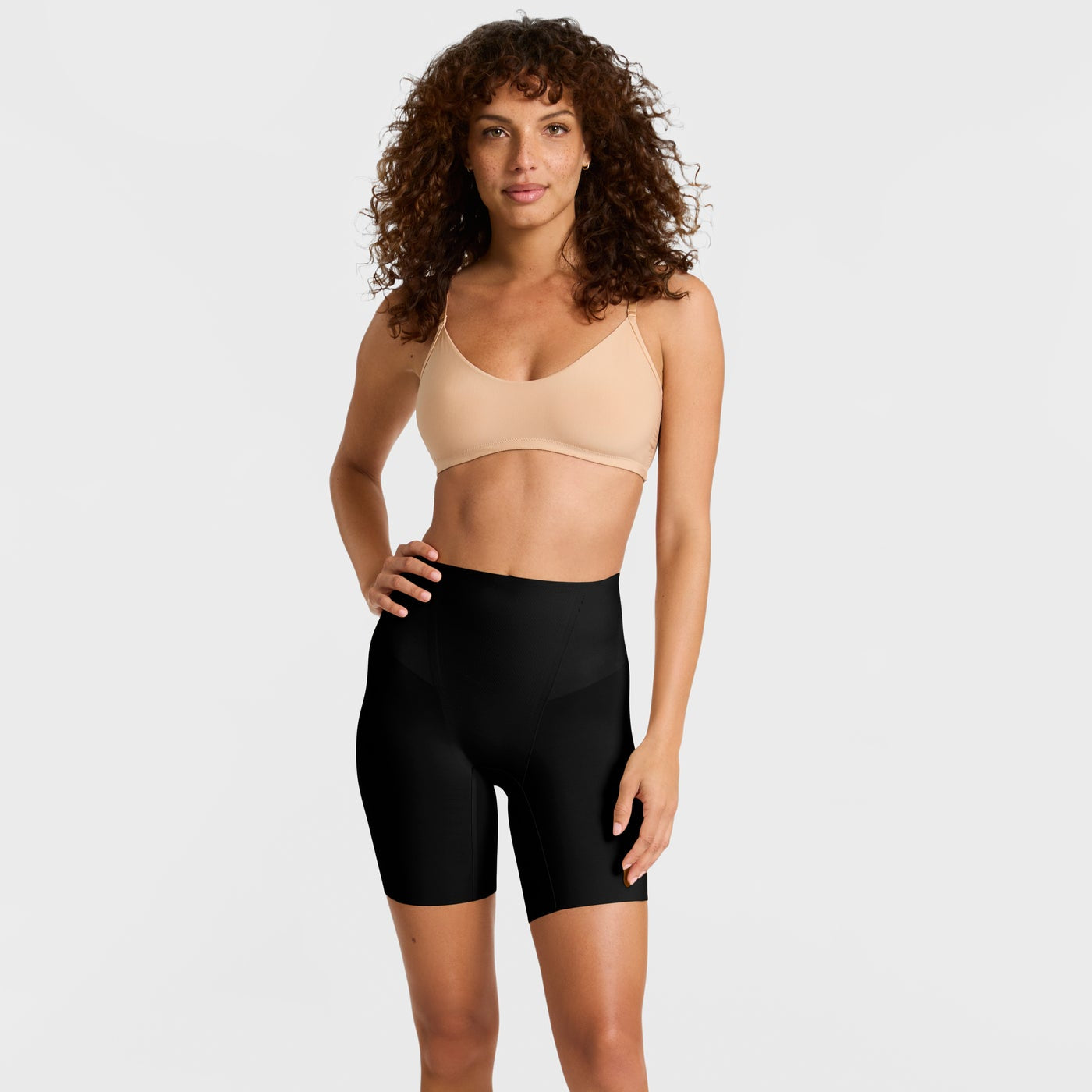 Woman wearing a beige bra and black shaper shorts on a white background