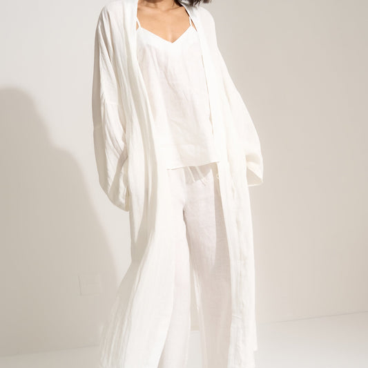 Woman wearing a white outfit with a flowing drape against a plain background