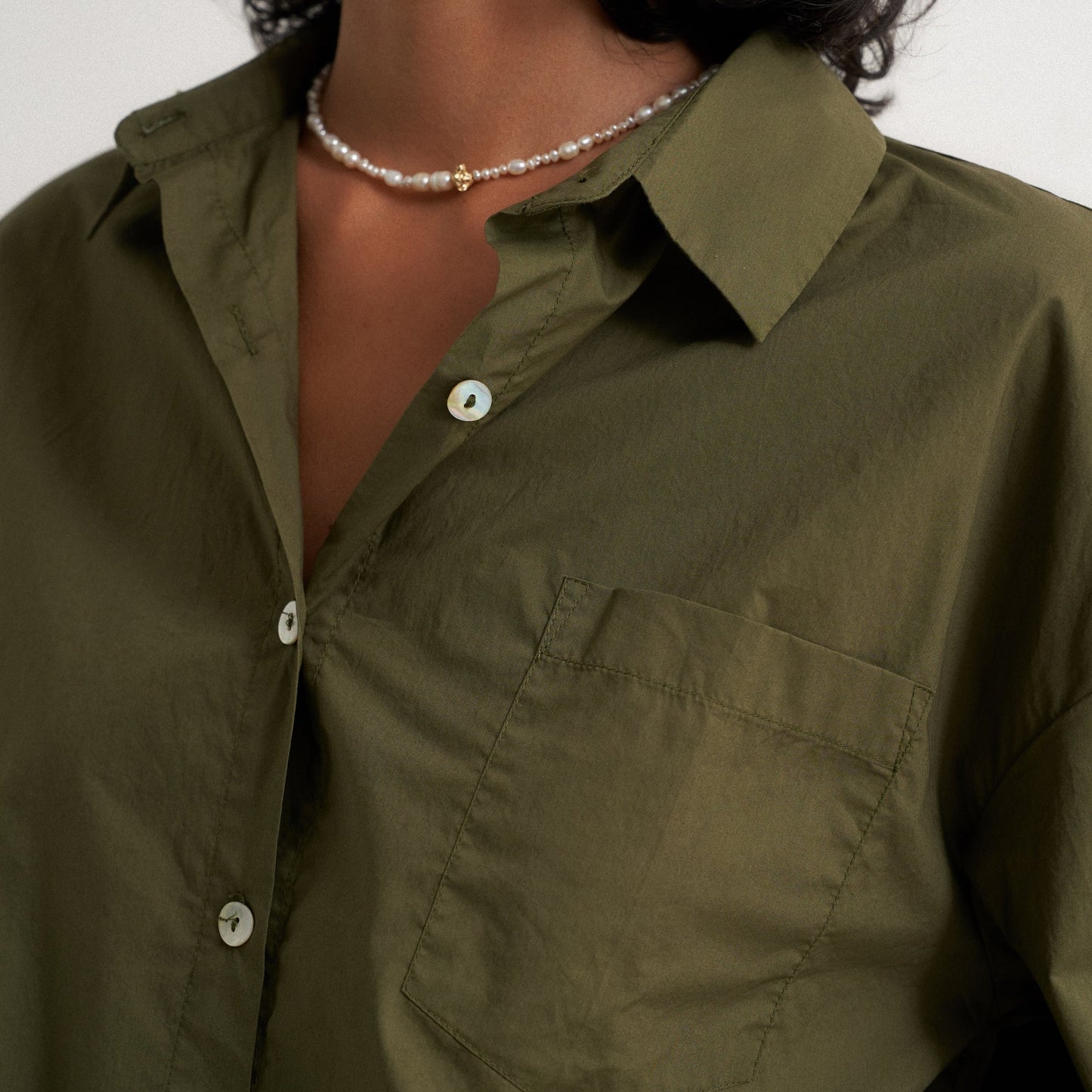 Person wearing a green shirt with a pearl necklace against a neutral background