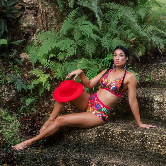 Woman in colorful outfit and red hat sitting on stone steps with greenery