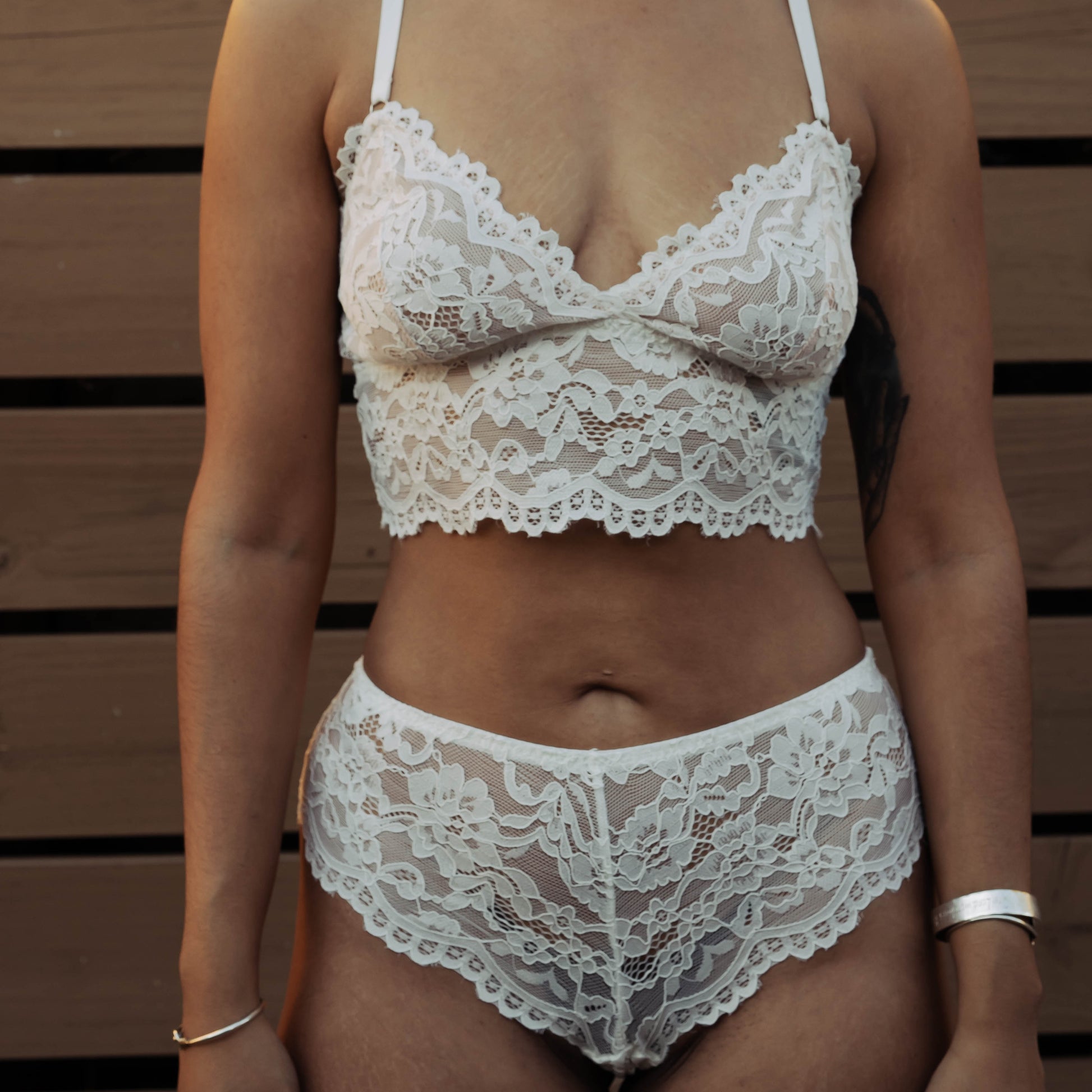 Woman wearing a white lace bra and panties set with a cowboy hat and sunglasses against a wooden background.