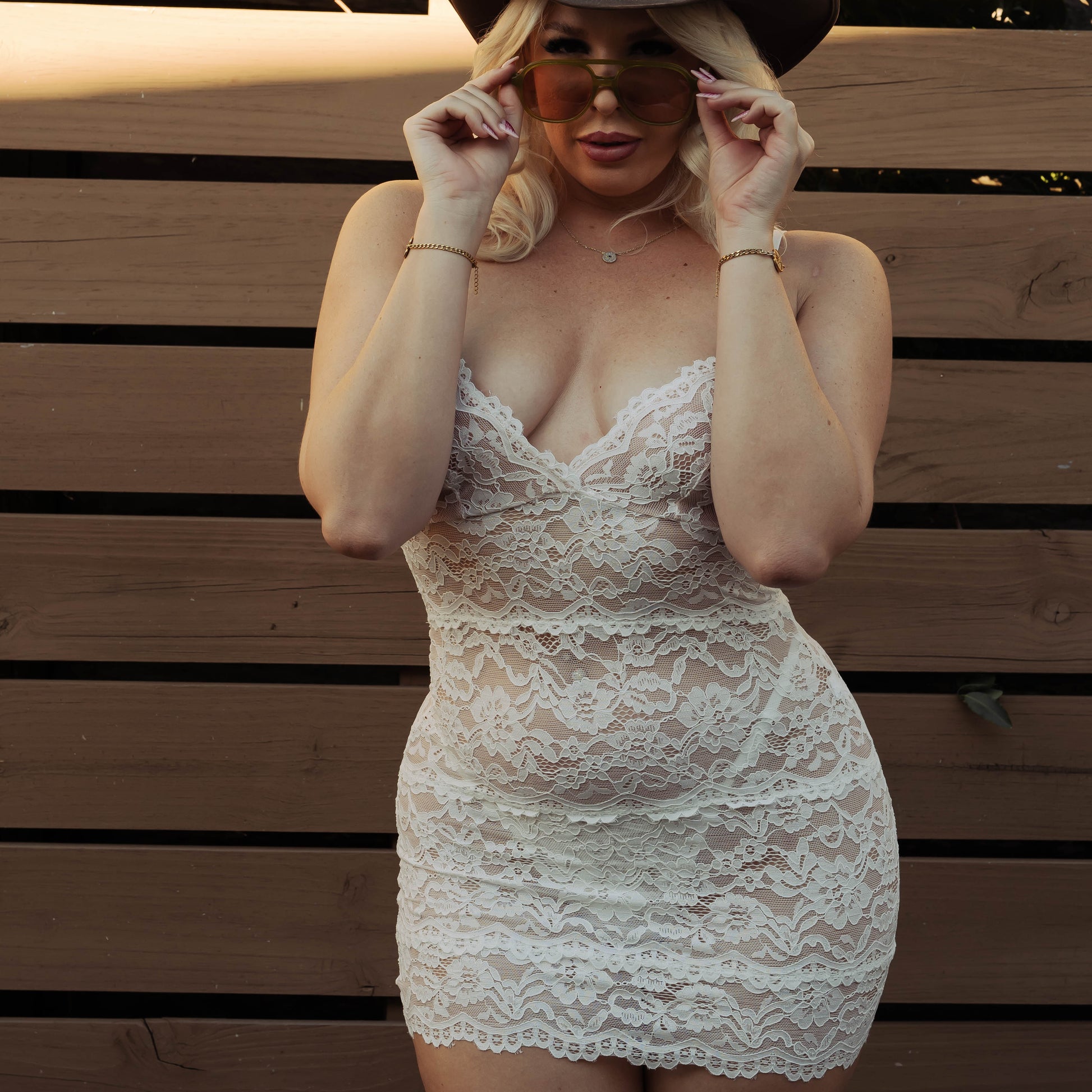 Person wearing a lace dress and cowboy hat in front of a wooden fence