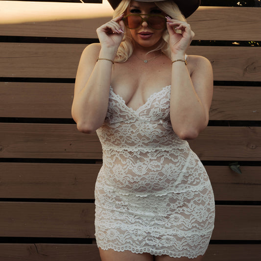 Person wearing a lace dress and cowboy hat in front of a wooden fence