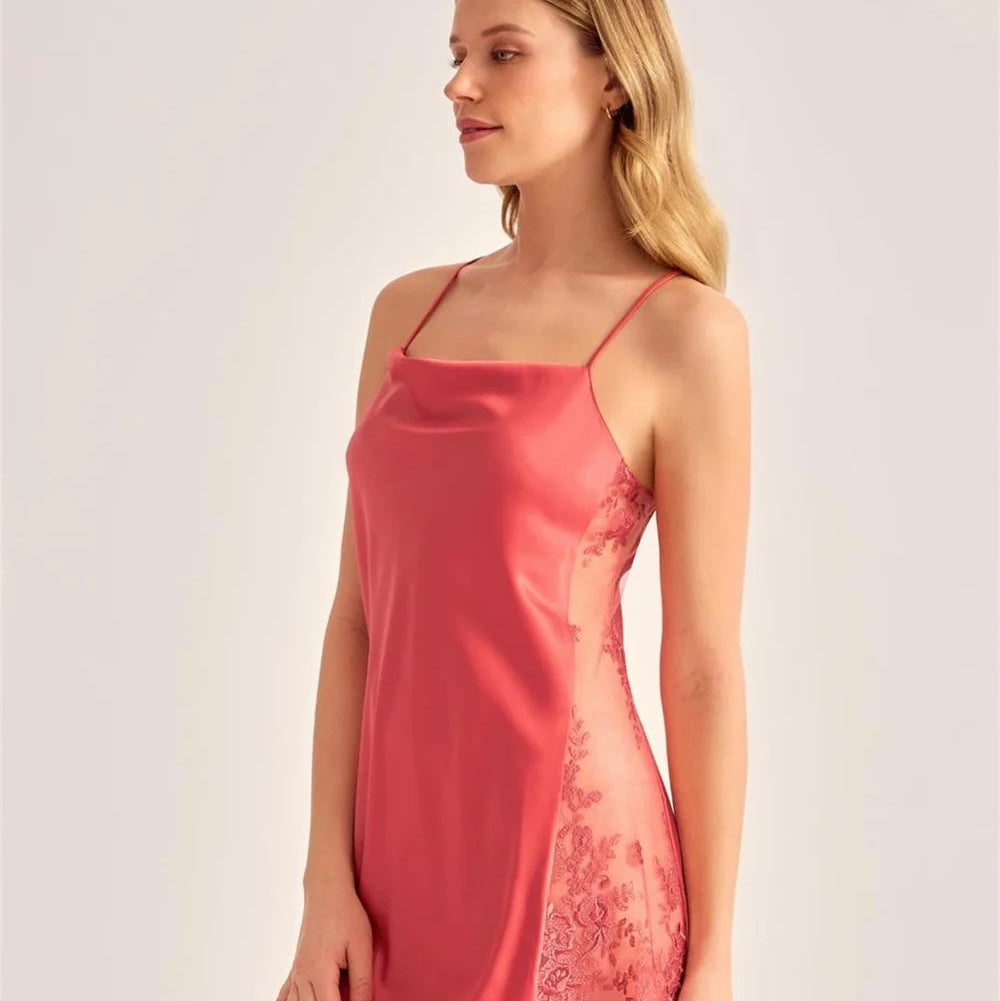 A woman modeling a short satin slip dress in a dusty rose pink color, featuring thin spaghetti straps and sheer lace side panels, set against a plain light gray studio background.