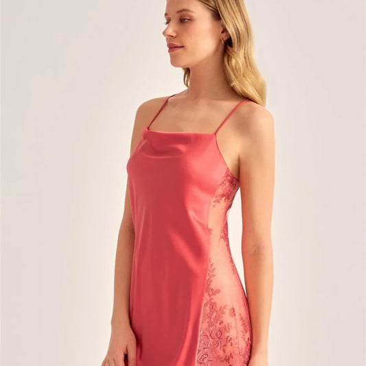 A woman modeling a short satin slip dress in a dusty rose pink color, featuring thin spaghetti straps and sheer lace side panels, set against a plain light gray studio background.