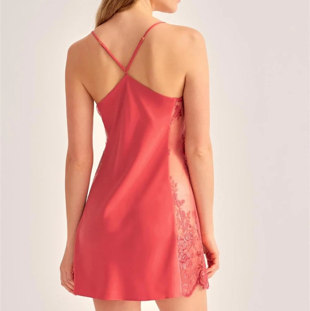 A woman shown from the back wearing a coral pink satin slip dress with lace side panels, photographed against a plain light gray studio background.